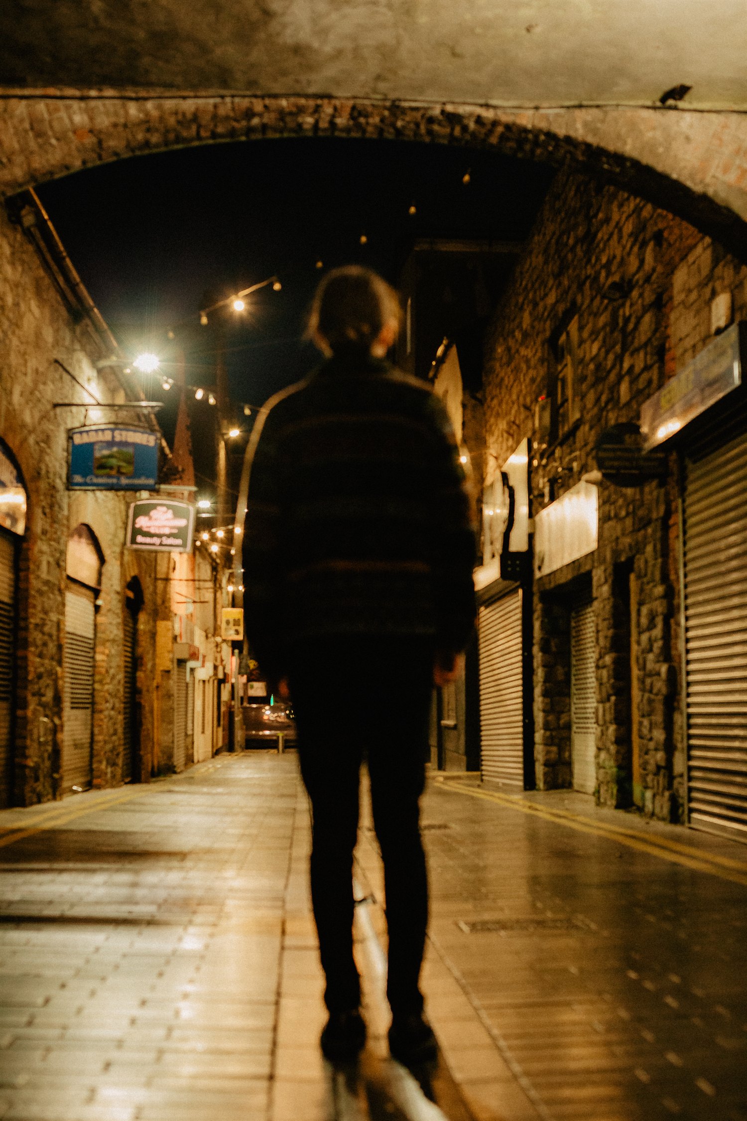 Sebastian Graysen from behind, walking away down a lit street at night